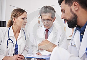Three doctors discussing medical records in doctorÃ¢â¬â¢s office photo